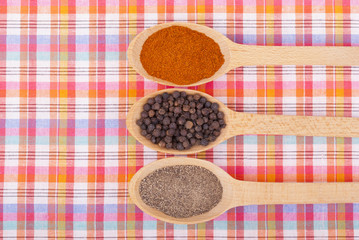 Whole and ground pepper in a wooden spoon on the tablecloth.