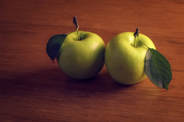 Two fresh green apples with leafs on wooden background