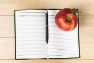 Red apple and open notebook with pan on wooden background