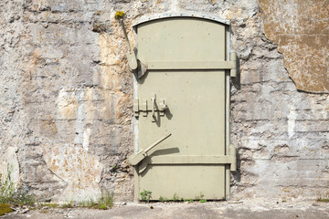 Green metal door in old fortification wall, background texture
