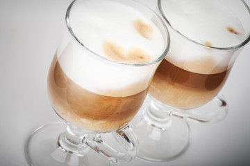 Two glass mugs with handles of latte coffee on gray background
