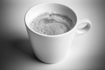 White cup of black coffee with foam, monochrome photo