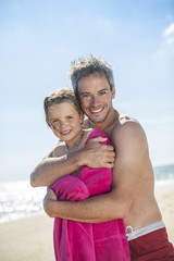 daddy at the beach wrapping his little girl in a towel after bat