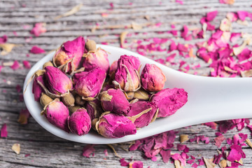 rose petals and dried flowers in spoon on old wooden table