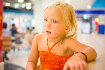 Adorable girl sit at table on chair on food court in mall