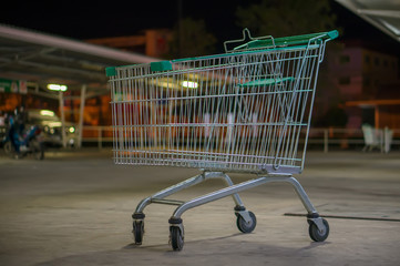 Empty shopping cart with green handle on parking near supermarke