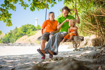 Mother, father and daughter embraces on rope swing under palm tr