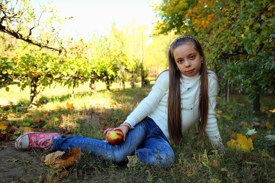 Girl  sitting in a park  with an apple in his hand.