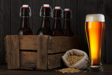 Beer glass  with wooden box full of bottles on table