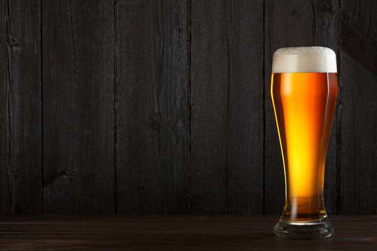 Glass of beer on wooden table, dark background