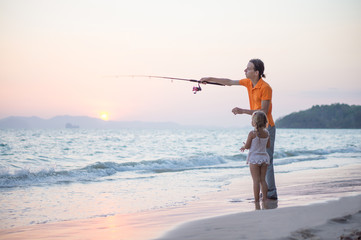 Father with adorable daughter fishing with rod on ocean beach on