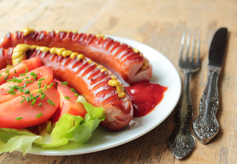 Two grilled sausages with fresh tomatoes and lettuce on barbecue