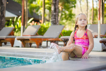 Adorable girl seat on  pool side at tropical beach splash water