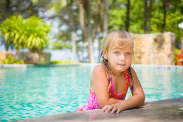 Adorable girl stay in water at side of swimming pool in tropical