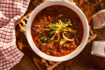 overhead photo of a bowl of chili with cheese and green onions - obrazy, fototapety, plakaty