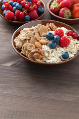 oatmeal, granola, nuts and berries in bowls on wooden background