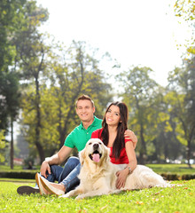 Obraz premium Young couple sitting in park with a dog