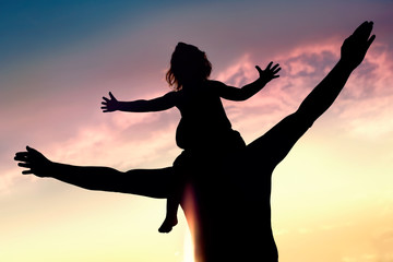 Silhouettes of happy father and daughter against sunset sky