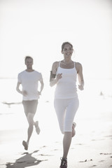 a dynamic couple is jogging on the beach, woman listening to mus