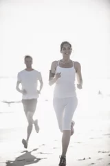 Wall murals Jogging a dynamic couple is jogging on the beach, woman listening to mus