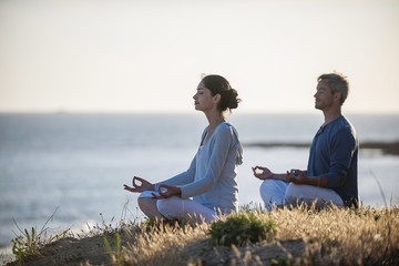 handsome couple practicing meditation exercises on the beach at - Powered by Adobe