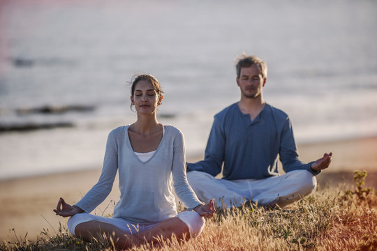 handsome couple practicing meditation exercises on the beach at