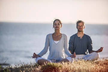 handsome couple practicing meditation exercises on the beach at