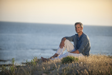 handsome man sitting on the beach at sunset
