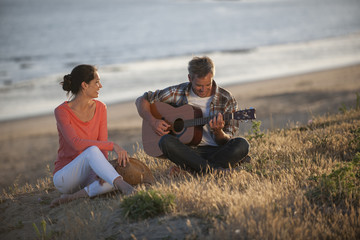 Romantic couple sitting on the beach at sunset with the man play