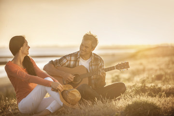 Romantic couple sitting on the beach at sunset with the man play