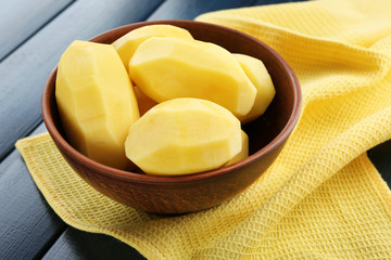 Raw peeled potatoes in bowl  on color wooden background