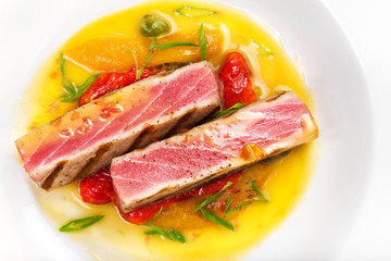 Grilled tuna steak with sauce, herbs and cherry tomatoes in a wh
