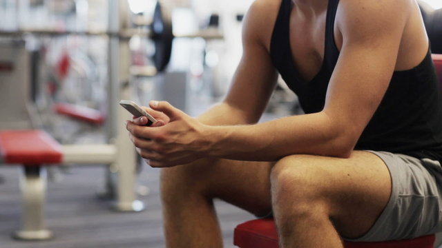 young man with smartphone computer in gym