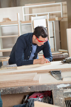 Carpenter Measuring Wood At Workbench