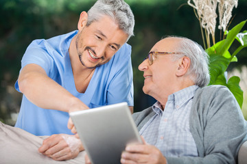 Smiling Nurse Assisting Senior Man Using In Tablet PC