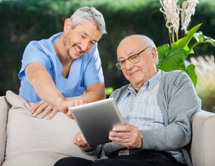 Happy Nurse Helping Senior Man In Using Tablet Computer