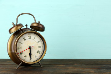 Old alarm clock on wooden table on blue background