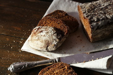 Sliced rye bread and knife on white napkin on wooden background