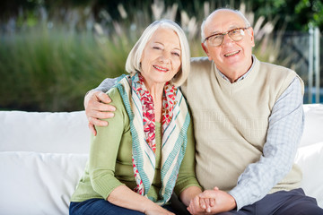 Happy Senior Man Sitting With Arm Around Woman On Couch