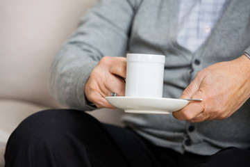 Midsection Of Senior Man Holding Coffee Cup On Couch