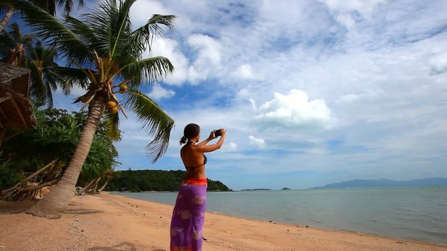 Woman in pareo taking picture of exotic beach with mobile phone