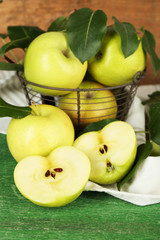 Ripe apples in metal basket with napkin on wooden background