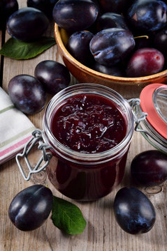 Plum jam and plums on wooden background.