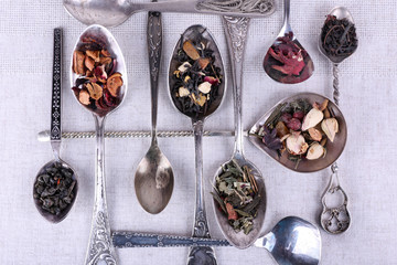 Tea in metal spoons on fabric background