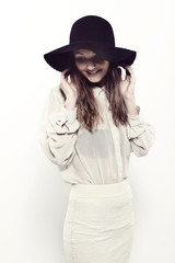 Fototapeta na wymiar Young woman in black hat looking down in studio, smiling