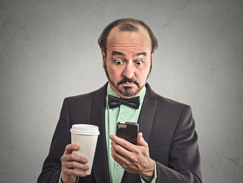 surprised man reading news on smartphone drinking coffee