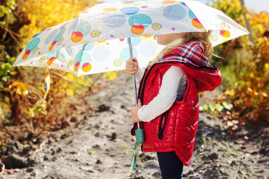 Little girl with umbrella in red vest outdoor