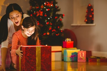 Fototapeta na wymiar Festive mother and daughter opening a glowing christmas gift