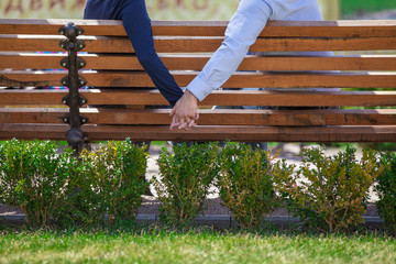 two people holding hands while sitting on bench.