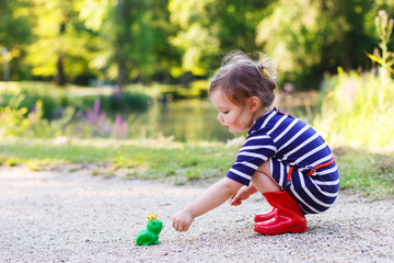 Cute princess girl in red rain boots playing with rubber toy fro